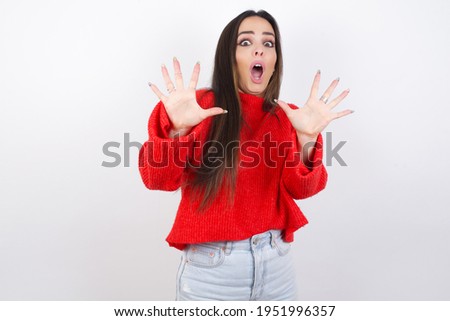 Dissatisfied young beautiful brunette woman wearing red knitted sweater frowns face, has disgusting expression, shows tongue, expresses non compliance, irritated with somebody.