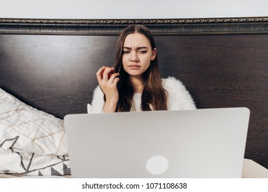 Dissatisfied Young Girl Lies In Bed And Watches Film On Laptop, Eats Apple