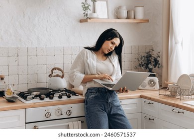 Dissatisfied young woman multitasking, reluctantly working on laptop and talking on the phone on a weekend on the kithen. Concept of discussions about work-life balance and remote work stress - Powered by Shutterstock