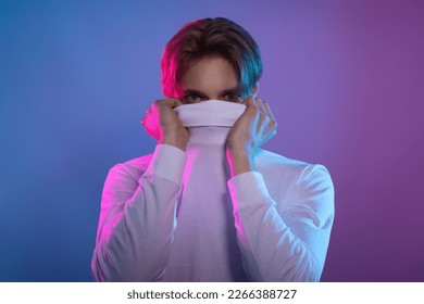 dissembled and introverted loner hide from world and feel shy for being unsocial while stand in blue and pink background with hands on collar and pull sweater over head