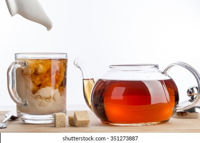 Dissolve Milk In A Cup Of Black Tea. Transparent Teapot And Cup With Three Cubes Of Brown Sugar