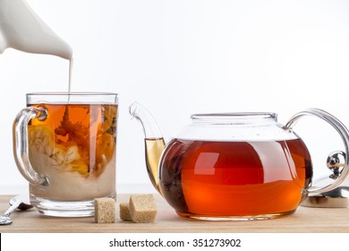 Dissolve Milk In A Cup Of Black Tea. Transparent Teapot And Cup With Three Cubes Of Brown Sugar On White Background