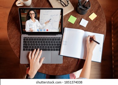 Distance Education Concept. Above top view of female student sitting at desk, writing in notebook, taking notes, using laptop, having online class with teacher. Remote studying from home, quarantine