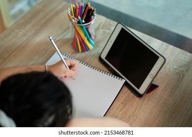 Distance Education Concept. Above Top View Of Female Student Sitting At Desk, Writing In Notebook, Taking Notes, Using Laptop, Having Online Class With Teacher. Remote Studying From Home, Quarantine