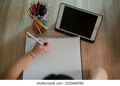 Distance Education Concept. Above Top View Of Female Student Sitting At Desk, Writing In Notebook, Taking Notes, Using Laptop, Having Online Class With Teacher. Remote Studying From Home, Quarantine