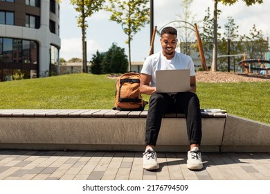 Distance education concept. Black male student with laptop sitting outdoors and watching educational webinar, wearing earpads and smiling, free space - Powered by Shutterstock