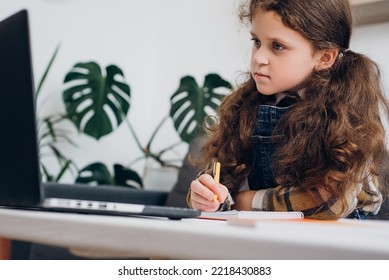 Distance Education Concept. Close Up Of Cute Little Girl Child Writing Notes Study With Laptop And Books, Serious Small Kid Doing School Tasks Sit On Couch At Home, Writing Notes, Listening To Lecture