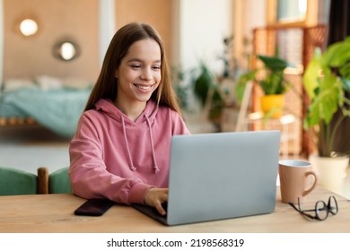 Distance Education Concept. Happy Teen Girl Sitting At Desk, Using Laptop And Watching Lecture Or Webinar, Studying Online At Home, Free Copy Space