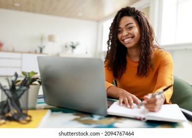 Distance Education  Portrait smiling woman sitting at desk  using laptop   writing in notebook  taking notes  watching tutorial  lecture webinar  studying online at home looking at screen