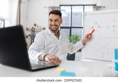 Distance Education, School And Science Concept - Happy Smiling Male Chemistry Teacher In Earphones With Laptop Computer Having Online Class And Showing Molecular Model On Flip Chart At Home Office