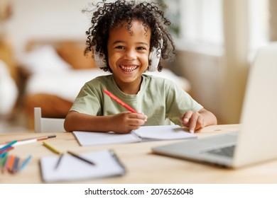 Distance education. Smiling african american child school boy in headphones studying online on laptop at home, sitting at table and communicating with teacher through video call on computer - Shutterstock ID 2076526048