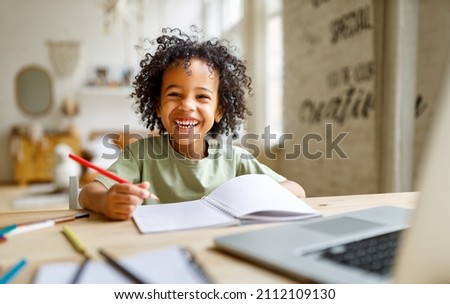 Distance education. Smiling african american child schoolboy  studying online on laptop at home, sitting at table and communicating with teacher through video call on computer