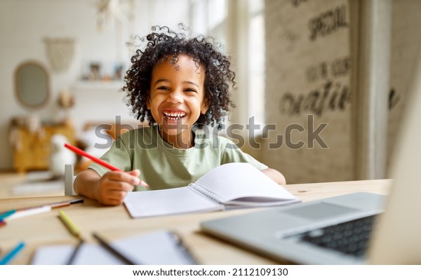 Distance\
education. Smiling african american child schoolboy  studying\
online on laptop at home, sitting at table and communicating with\
teacher through video call on\
computer