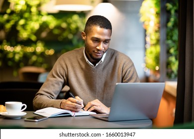 Distance Education. Young black bearded student learning online at the bar, looking at laptop and taking notes