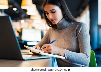Fernunterricht. Schöne lächelnde Frau in weißem Hemd funktioniert vor dem Laptop. Ein Student bereitet Seminar vor, schreibt Notizen in Notebook, sucht Informationen im Internet, nutzt das Internet, online, 
