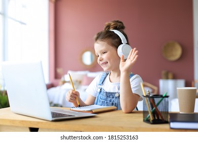 Distance learning. Cheerful little girl girl in headphones using laptop studying through online e-learning system. - Shutterstock ID 1815253163