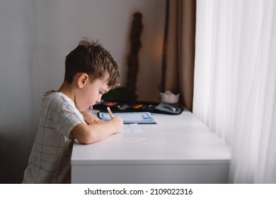 Distance learning education. Back to school. Cute kid boy studying at home and doing school homework. Thinking child sitting at table