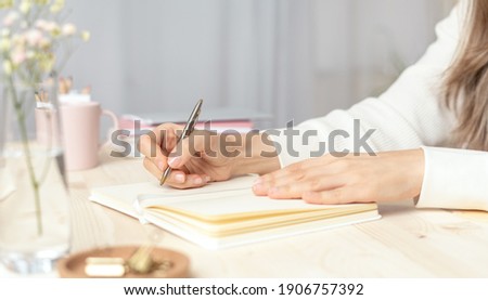 Distance learning, education and work. Woman hand holding pen on notepad at home, writes goals, plans, make to do and wish list on desk, working from home office.