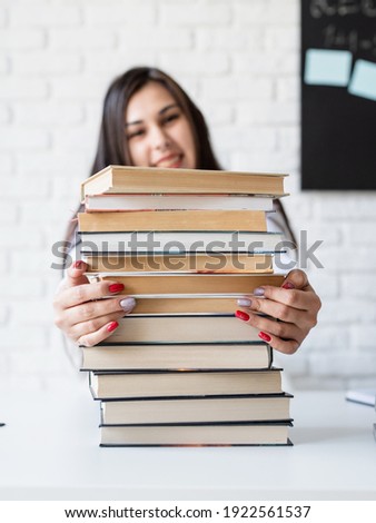 Distance learning. E-learning. Young teacher sitting with pile of books looking away ready for lesson