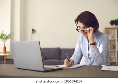 Distance Learning At Home. Woman Looking At Laptop Computer Screen Takes Off Glasses In Surprise. Adult Student With Attention To Detail Studying New Information In Online Continuing Education Webinar