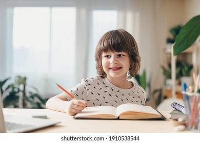 Distance Learning Online Education. Caucasian Smile Kid Boy Studying At Home With Laptop, Writing In Notepad And Doing School Homework. Thinking Child Siting At Table With Notebook. Back To School.