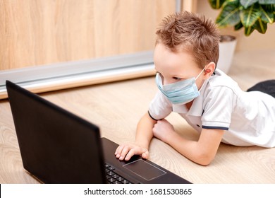 Distance Learning Online Education. A Schoolboy In A Protective Mask Lies On The Floor Studying At Home With A Laptop And Doing School Homework. The Child Does Not Look At The Camera.