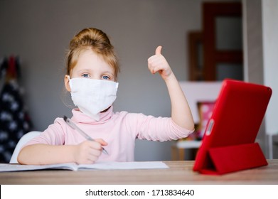 Distance Learning Online Education. Sickness Schoolgirl In Medical Mask Studying At Home With Digital Tablet And Doing Homework, Raised Her Thumb Up. Training Books And Notebooks On Table