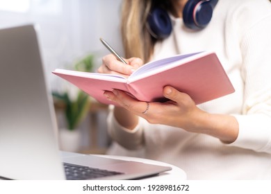 Distance learning online education and work. Business woman with headphones writes in notebook. Cropped freelance girl with laptop at home office. Using computer and online shops. Focus on hand