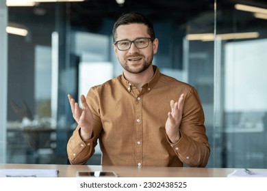 Distance Learning. Smiling young male teacher, tutor, trainer sitting in office, campus in front of camera and teaching, giving lectures, lessons online via video call. - Powered by Shutterstock