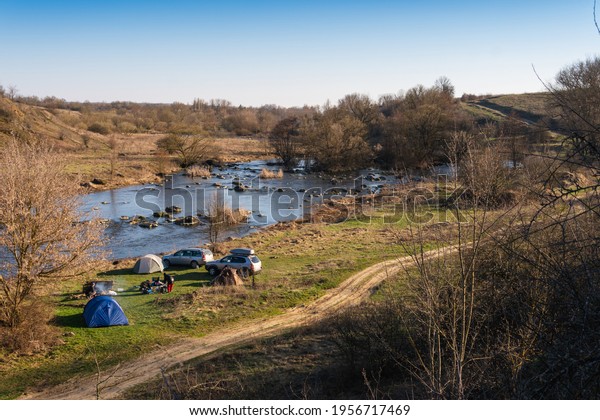 Distance view. Copy space. Morning landscape\
with a tents and 4wd cars, the river bank and rocks in the\
background. Spring camping. Tourism and\
vacation.
