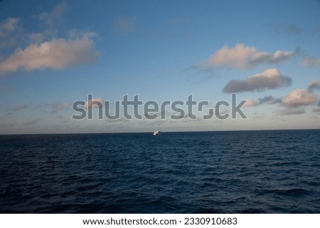 A Distant Boat Amidst the Dark Blue Ocean, under Light Blue Skies with Floating Clouds