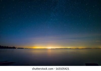 Distant City Lights Over Water With Stars