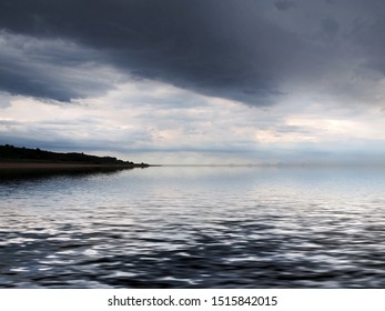 a distant coast reflected in the sea with dramatic dark storm clouds
