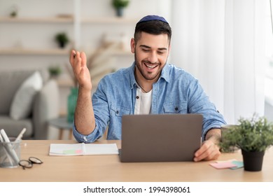 Distant Communication Concept. Portrait of happy jewish male in yarmulke and casual shirt making video call sitting at desk at home office and talking with colleagues, students or family, explaining