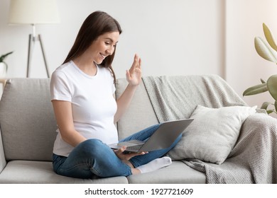 Distant Communication. Happy Pregnant Lady With Laptop At Home Making Video Call While Resting On Sofa In Living Room, Friendly Expecting Woman Waving Hand At Web Camera, Greeting Somebody, Free Space