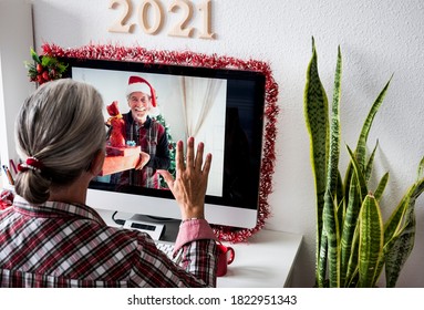 A distant couple on a video call from home for Christmas greetings. The man shows many gift packages while the woman raises her hand in greeting - Powered by Shutterstock