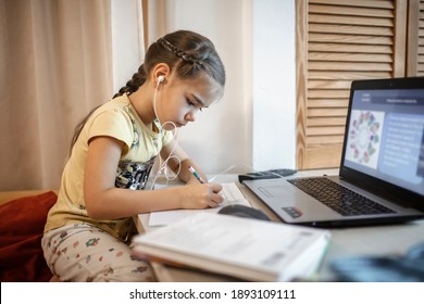 Distant education, online class meeting. Pretty schoolgirl in formal shirt but in pajama trousers studying during online lesson at home, social distance during quarantine, self-isolation
