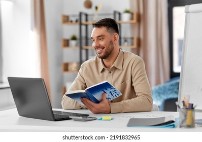 Distant Education, School And Remote Job Concept - Happy Smiling Male Math Teacher With Laptop Computer, Book And Flip Chart Having Online Class Or Video Call At Home Office