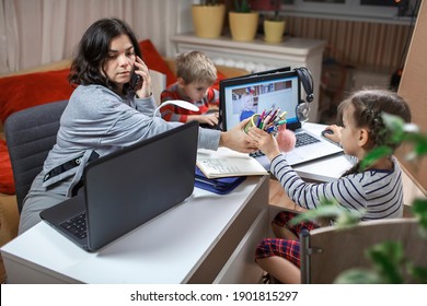 Distant Education And Work At Home, Children Doing Homework And Mother Working And Help Them. Elementary School Kids During Online Class With Parent Working Remotely In One Room During Lockdown