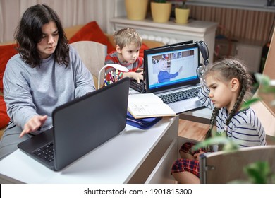 Distant Education And Work At Home, Children Doing Homework, Mother Working And Help Them. Elementary School Kids During Online Class With Parent Working Remotely In One Room, Lockdown, Focus On Woman