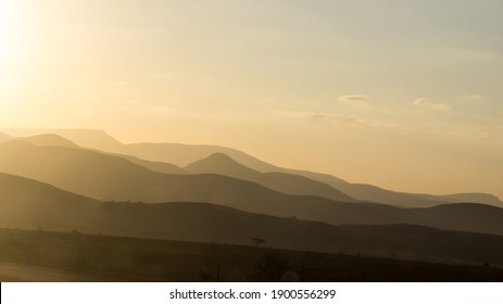 Distant hazy mountains, colored different shades of pink and grey by the setting sun, in the Great Escarpment of South Africa