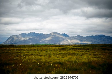 Distant Icelandic Mountain Range Under Dramatic Cloudy Sky Across Green Grassland