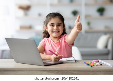 Distant Learning. Little Arab Girl Showing Thumb Up While Study With Laptop At Home, Smiling Female Child Sitting At Table With Computer In Living Room, Recommending Online Education, Copy Space