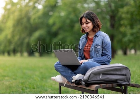 Distant Learning. Young Arab Female Student Using Laptop While Sitting On Bench Outdoors In Park, Smiling Middle Eastern Woman Watching Educational Webinar, Enjoying Remote Study, Copy Space