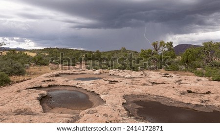 A distant lightning bolt drops from the heavy storm clouds over a mesa top in Utah's southwest desert while ephemeral pools on the sandstone surface wait for more rain to refill them. 