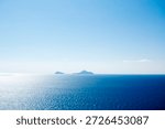 Distant panoramic view of the three islands Cristiana, Askania, and Eschati under clear blue sky, surrounded by calm blue waters in daylight.