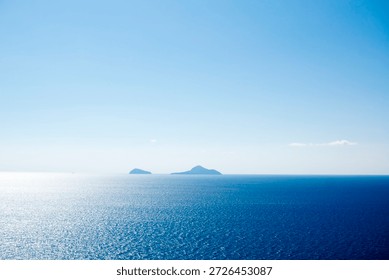 Distant panoramic view of the three islands Cristiana, Askania, and Eschati under clear blue sky, surrounded by calm blue waters in daylight.