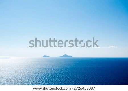 Distant panoramic view of the three islands Cristiana, Askania, and Eschati under clear blue sky, surrounded by calm blue waters in daylight.