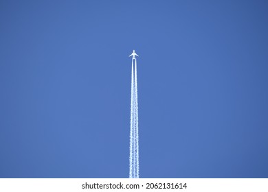 Distant passenger jet plane flying on high altitude on clear blue sky leaving white smoke trace of contrail behind. Air transportation concept.