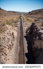 Distant train approaching on straight desert railway tracks